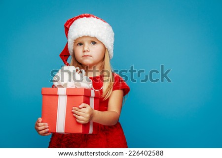 Smiling funny child (kid, girl) in Santa red hat holding Christmas gift in hand. Christmas concept.