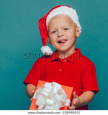 Smiling funny child (kid, boy) in Santa red hat holding Christmas gift in hand. Christmas concept.