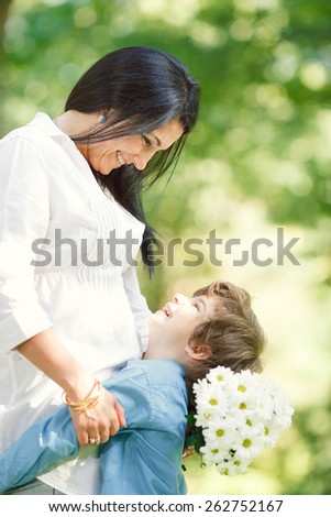 Cheerful smiling boy (child, kid) and woman with bouquet of  flowers playing on spring park. Mother`s day concept