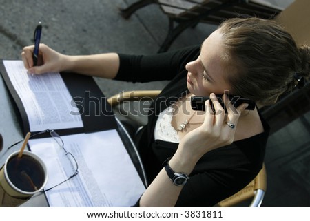 Young woman doing paperwork and talking on cell phone at cafe.
