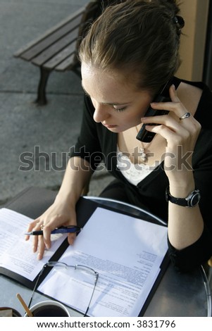 Young woman doing paperwork and talking on cell phone at cafe.