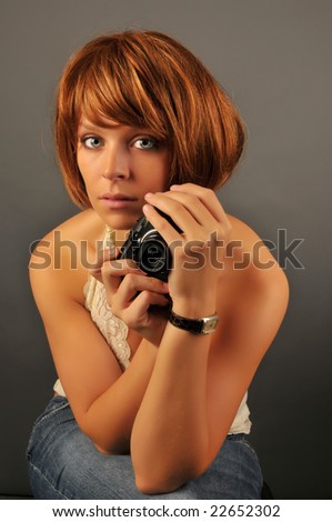 Portrait of beautiful woman with red hair holding a compact camera with gray background.