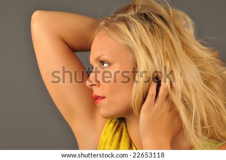 Close portrait of beautiful blonde woman with hands in hair on gray background.