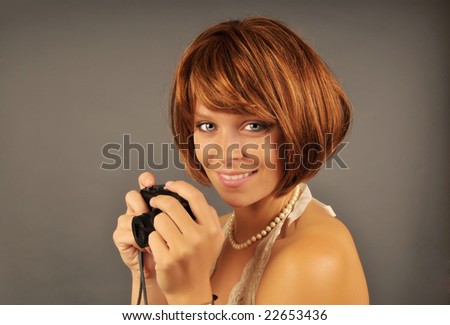 Portrait of a beautiful woman with red hair holding a compact camera with a gray background.