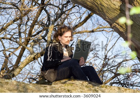 Man with portable computer siting on tree.