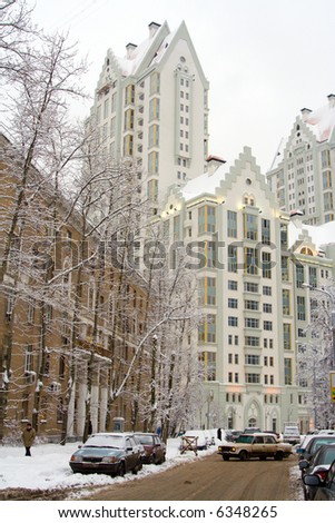 City in winter: snow-covered trees, cars, roadway and white multistorey building at the end of the street