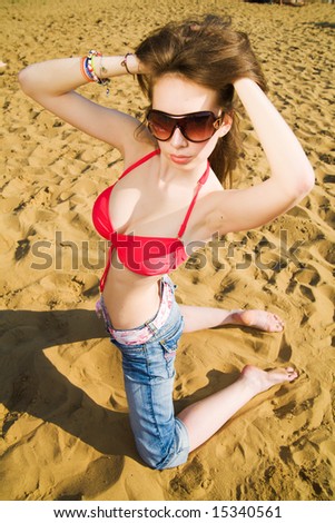 Young beautiful woman in red bikini, jeans and sunglasses at beach