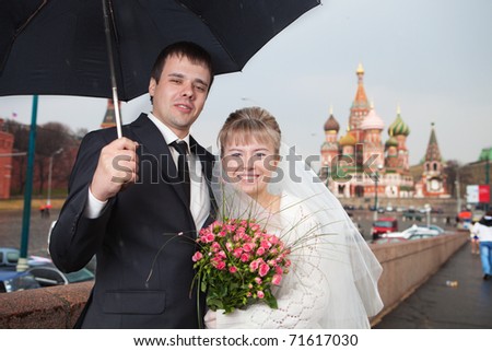 The newly married couple under the rain at Moscow near Kremlin. The Cathedral of the Virgin Protectress at background