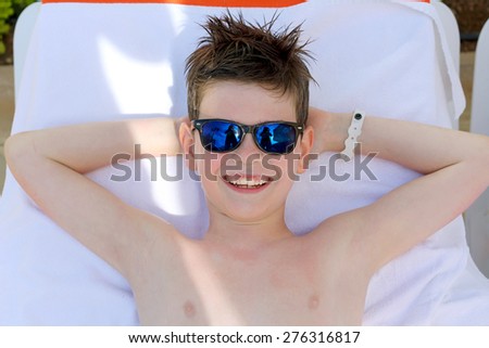 Boy in sunglasses lying in the sun bed outside