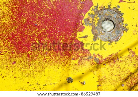 A bolt hole in an old truck panel with mixed red and yellow chipping paint.