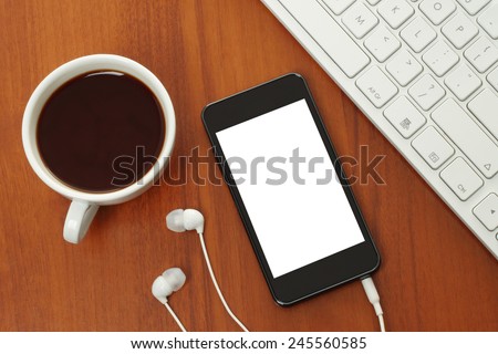 Smart phone with headphones, keyboard and coffee cup on wooden background