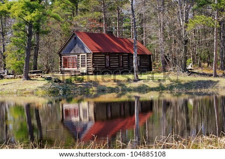 Old Log Cabin reflection in a pond. Michigan forest USA