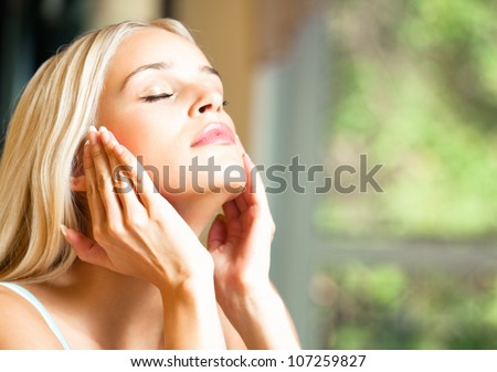 Portrait of young happy smiling cheerful beautiful blond woman applying creme, at home, with copyspace