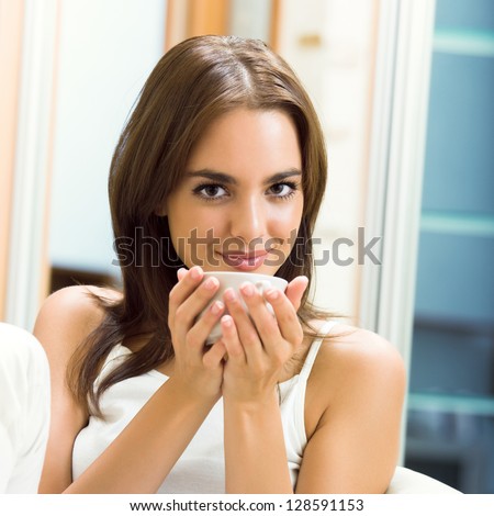 Portrait of young happy smiling woman drinking coffee, at home