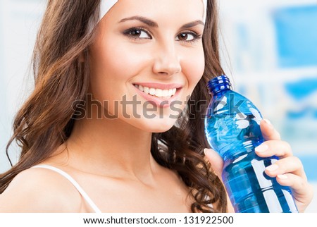 Portrait of cheerful young attractive woman drinking water, at fitness club or gym