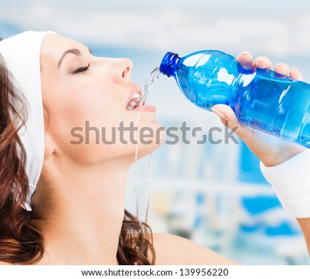 Portrait of cheerful young attractive woman  drinking water, at fitness club or gym