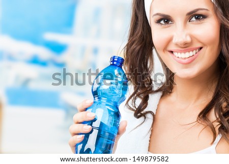 Portrait of cheerful young attractive woman with bottle of water, at fitness club or gym