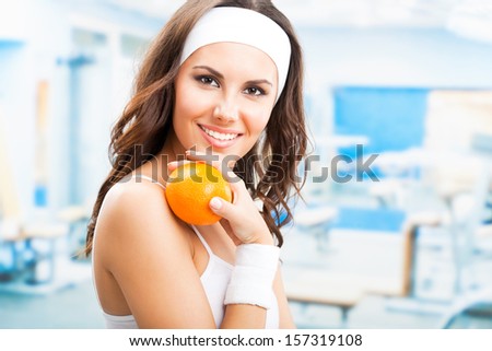Cheerful young beautiful woman with orange, at fitness center or gym