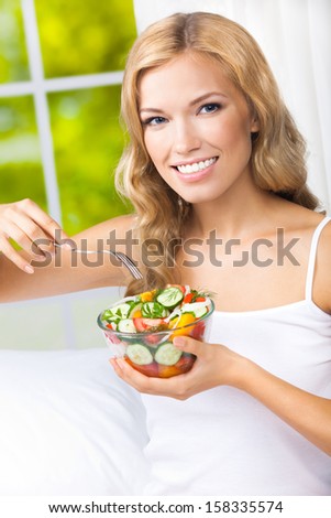 Portrait of happy smiling young woman with vegetarian vegetable salad, indoors