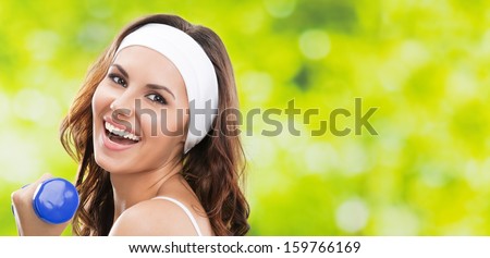 Portrait of cheerful woman in fitness wear exercising with dumbbell, outdoors, with copyspace