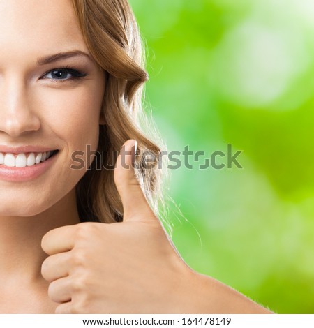 Portrait of beautiful young happy smiling blond woman with thumbs up gesture, outdoors