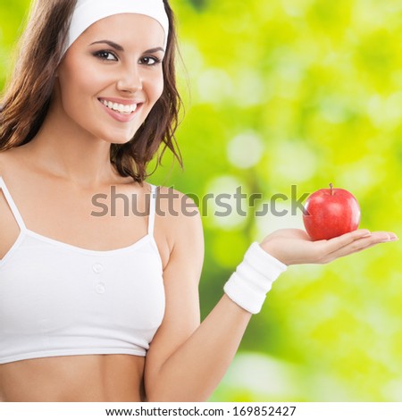 Portrait of happy smiling young beautiful woman in fitness wear with apple, outdoors