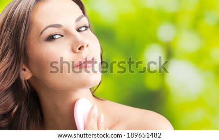 Portrait of happy smiling beautiful young woman cleaning skin by cotton pad, outdoor