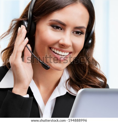 Portrait of happy smiling cheerful young support phone operator in headset, working with laptop, at office