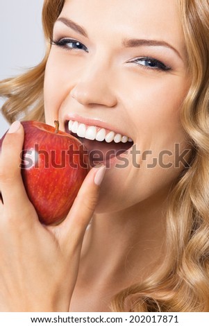 Portrait of happy smiling young beautiful woman eating red apple, over gray background