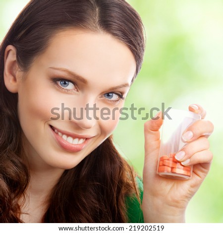 Portrait of happy smiling woman showing bottle with pills, outdoor
