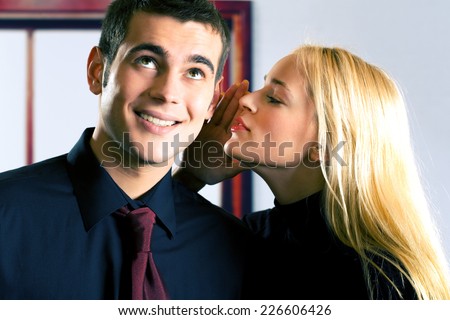 Two young attractive happy smiling business people or couple telling a secret, indoors