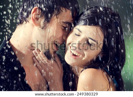 Young amorous couple hugging and kissing under a rain, outdoors