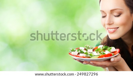 Young beautiful smiling woman with plate of salad, outdoor, with copyspace area for slogan or text