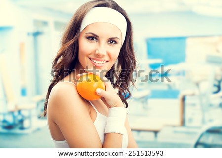 Portrait of happy smiling beautiful woman with orange, at fitness center or gym