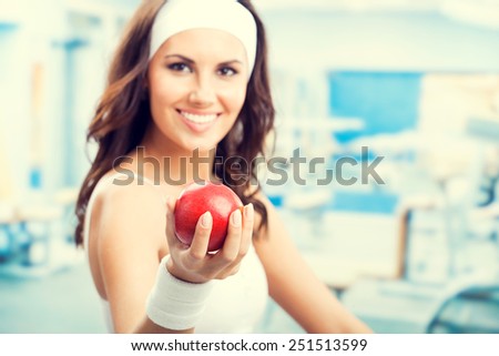 Portrait of happy smiling beautiful woman with red apple, at fitness center or gym, selective focus on hand.