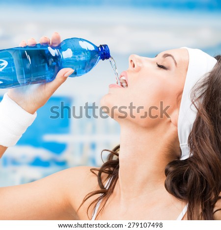 Young attractive woman drinking water, at fitness club or gym
