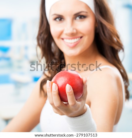 Happy woman giving red apple, at fitness center or gym, selective focus on hand.
