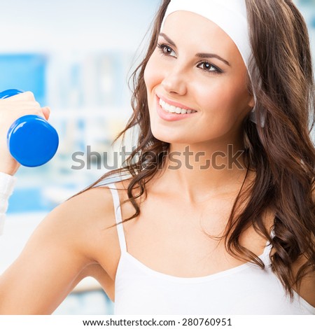 Cheerful smiling woman in fitness wear exercising with dumbbell, at fitness center or gym