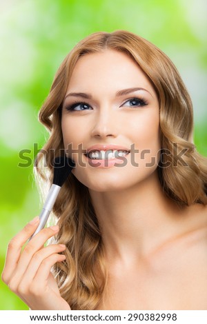 Portrait of young happy smiling blond woman with make up brush, outdoor. Beauty, visage and cosmetics concept.