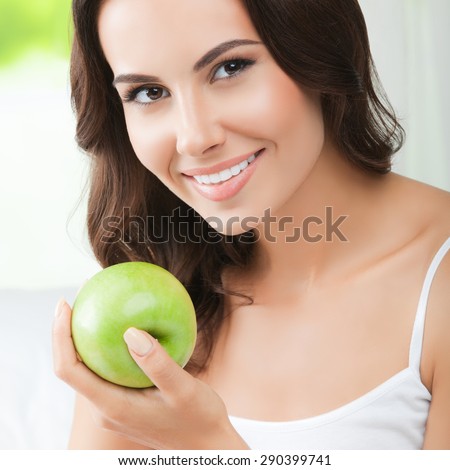 Young happy smiling brunette woman with green apple, indoors. Healthy eating, beauty and dieting concept.