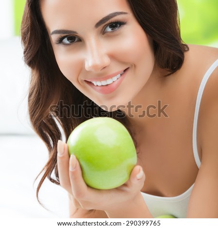 Young happy smiling brunette woman with green apples, indoors. Healthy eating, beauty and dieting concept.