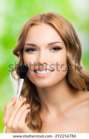 Portrait of happy smiling woman with make up brush, outdoor. Beauty, visage and cosmetics concept.