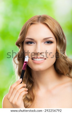 Portrait of young cheerful woman with make up brush, outdoors. Beauty, visage and cosmetics concept.