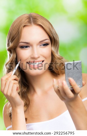 Portrait of young happy smiling blond woman with make up brush and mirror, outdoors. Beauty, visage and cosmetics concept.