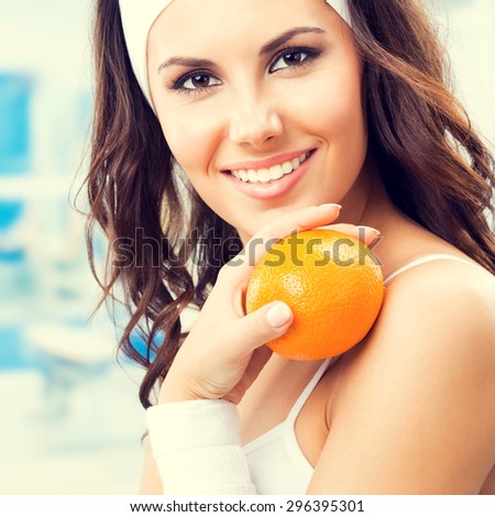 Portrait of happy smiling lovely woman with orange, at fitness center or gym