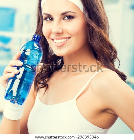 Happy young lovely woman with bottle of water, at fitness club or gym
