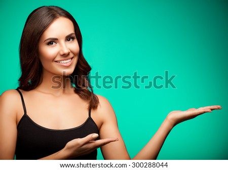 Portrait of smiling young woman in black casual clothing, showing something or blank copyspace area for slogan or text message, on green background