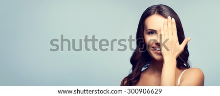 Concept photo of happy smiling young woman in white tank top clothing with one eye, closed by hand, covering part of her face, with blank copyspace area for text or slogan