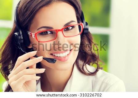 Portrait of cheerful young brunette businesswomen, support phone female operator or call center worker, in headset and glasses. Help and consulting concept.