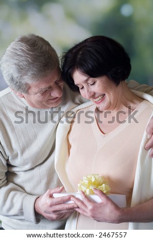 Elderly happy couple with gift box, smiling and embracing